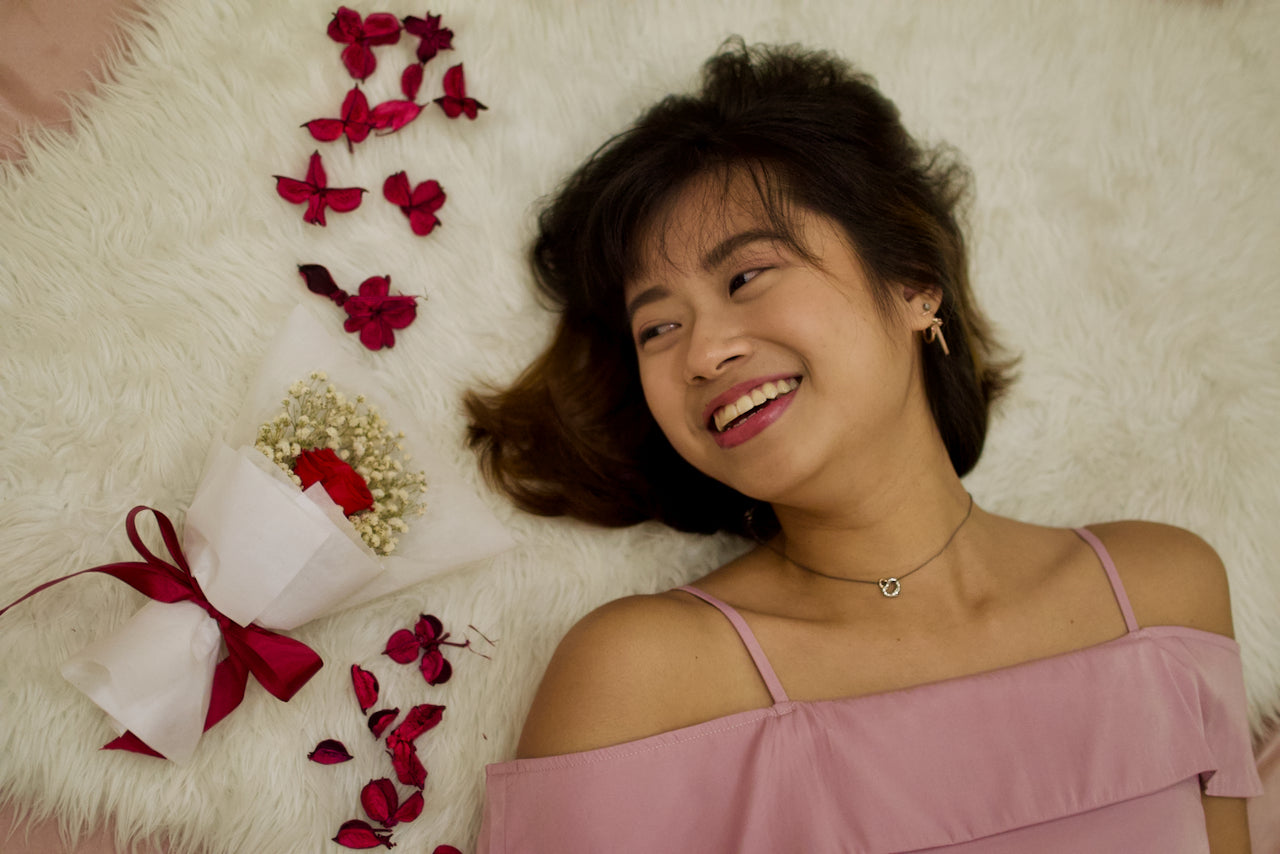 Smiling woman in a pink dress with a bouquet of flowers and red petals on a white rug