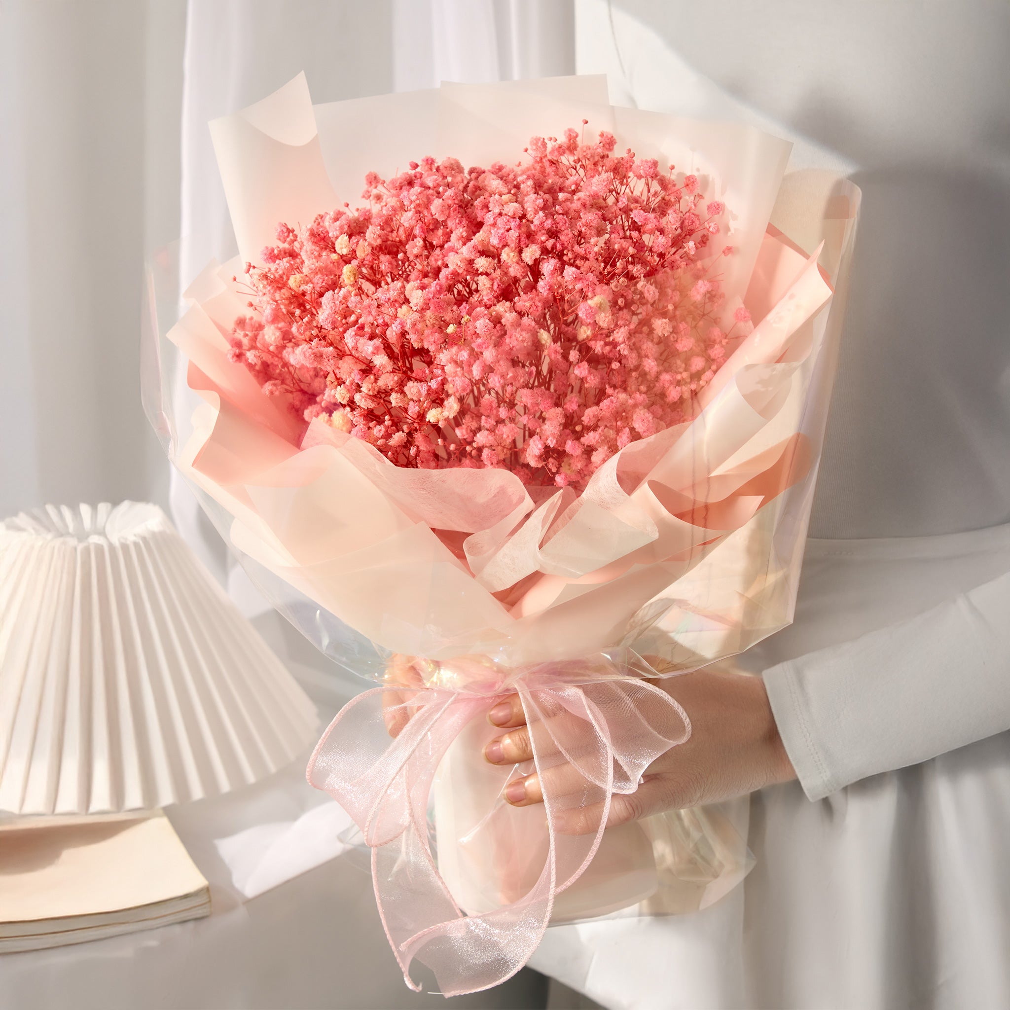 Bouquet of pink baby's breath flowers wrapped in tissue paper held by a person.