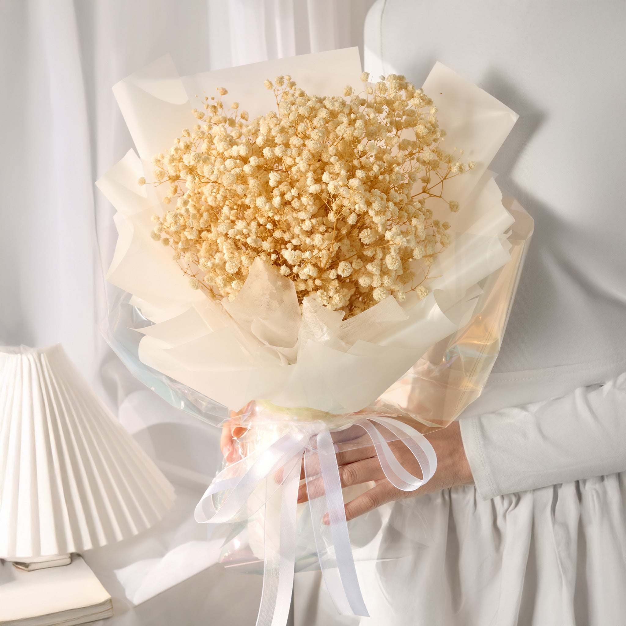 Bouquet of white baby's breath wrapped in white paper with a ribbon, held by a person in a light setting.