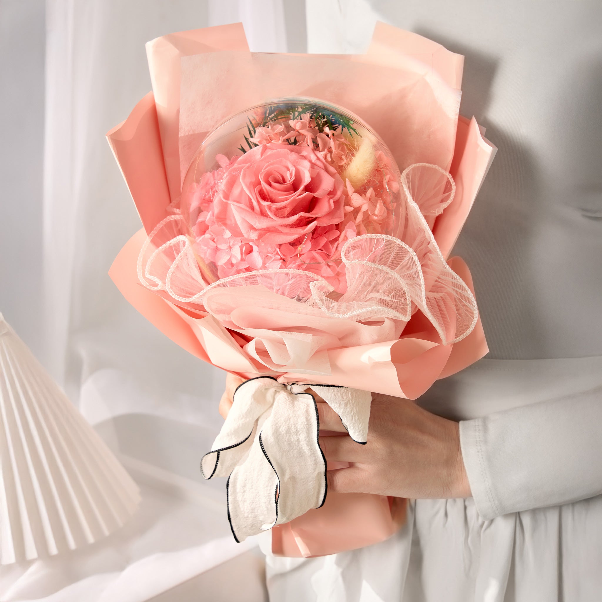 Bouquet of pink rose wrapped in peach-colored paper held by a person.