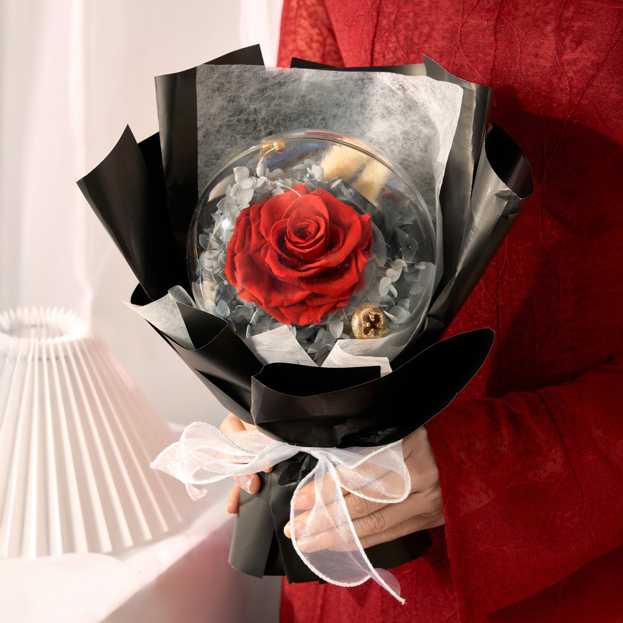 Bouquet with a red rose encased in clear acrylic ball, held by a person wearing a red dress.