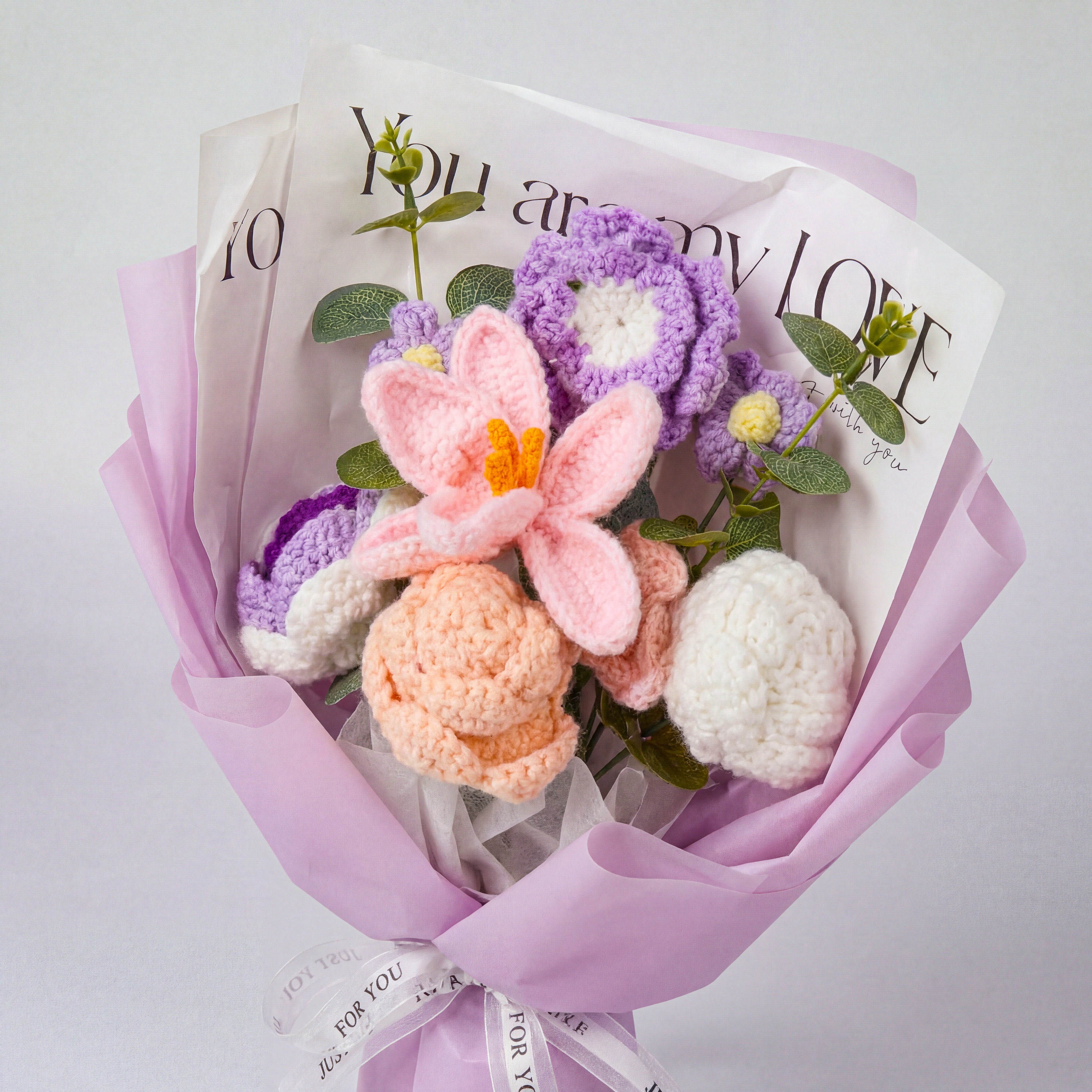 Bouquet of crocheted flowers with a magazine textured wrapping paper on a light gray background