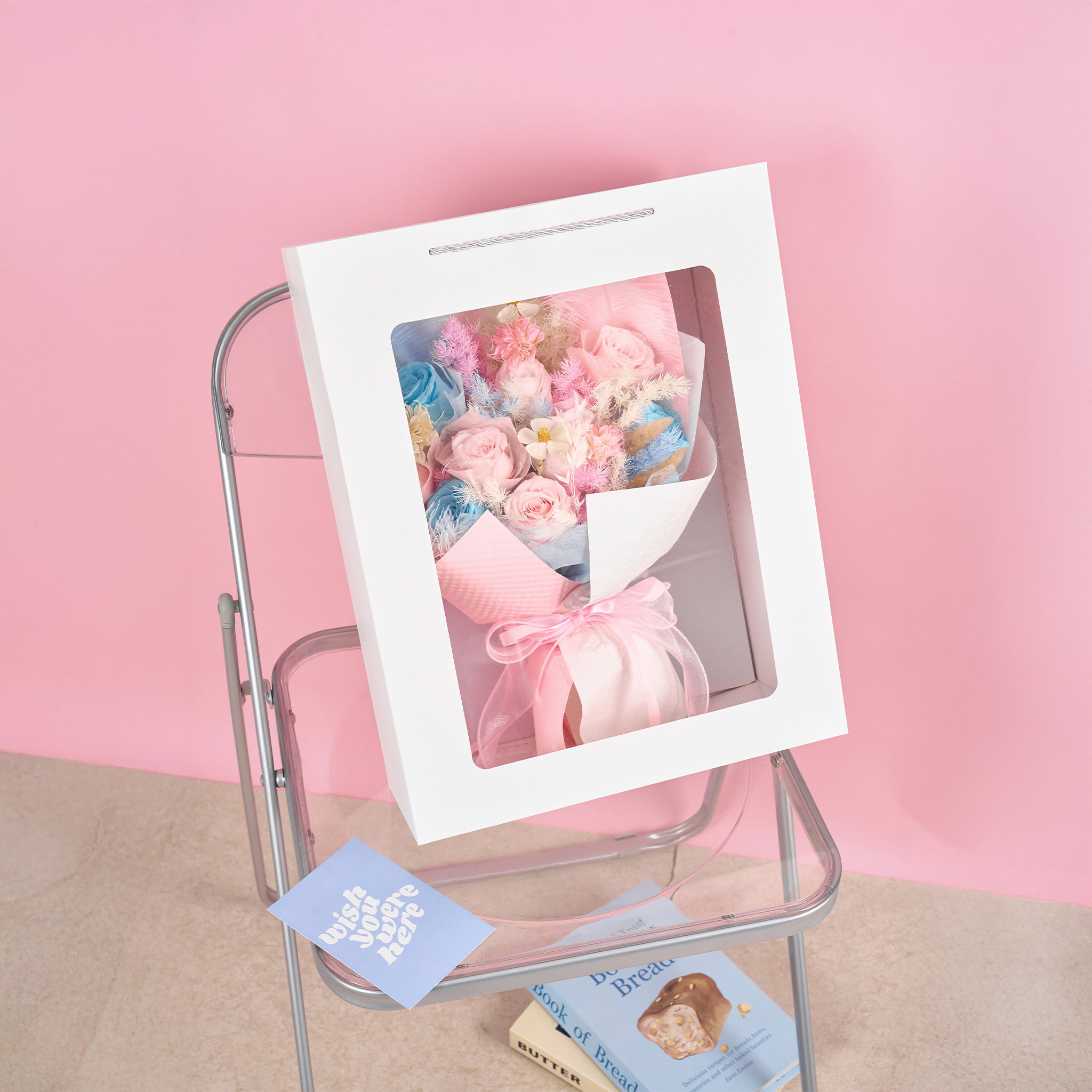 A bouquet of flowers in a box on a metal chair with a pink background