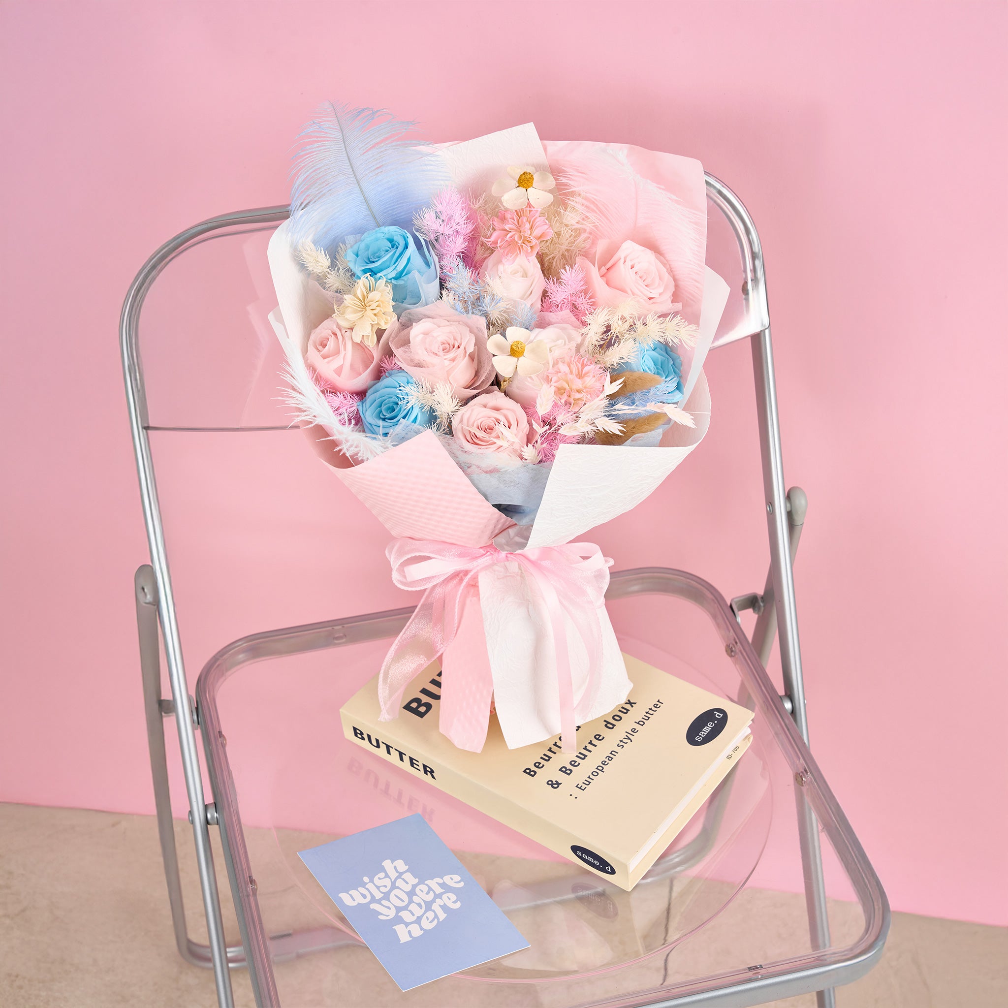 Bouquet of flowers with a pink ribbon on a small metal chair against a pink background