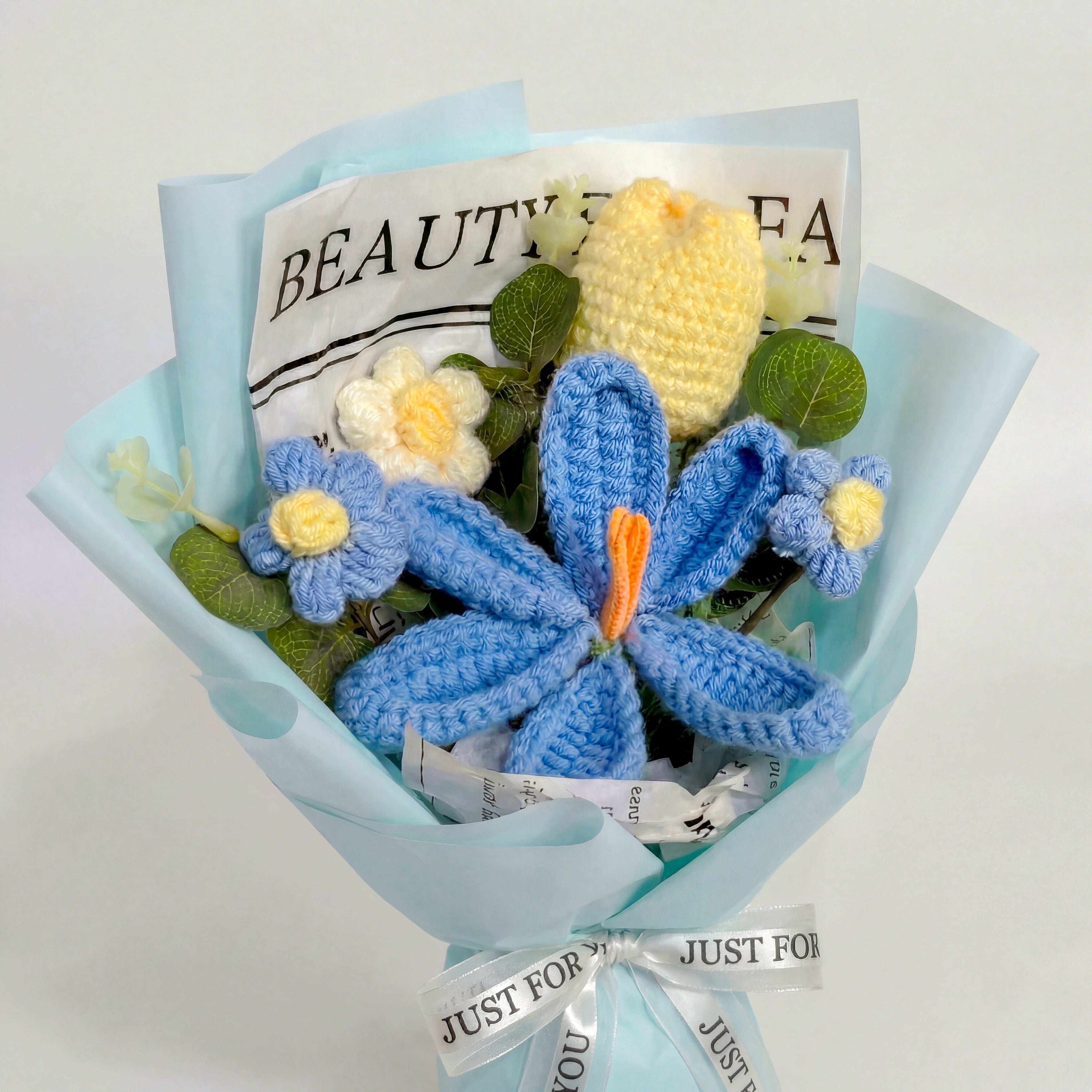 Bouquet of crocheted flowers in blue and yellow with a decorative paper wrap on a light gray background.